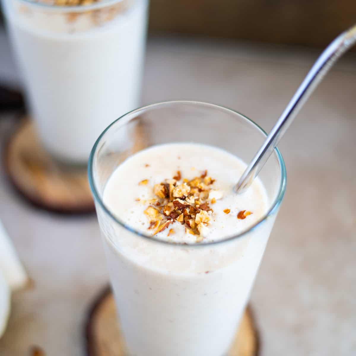 close-up of a rice syrup solids almond power smoothie in a glass, garnished with sliced almonds and a straw