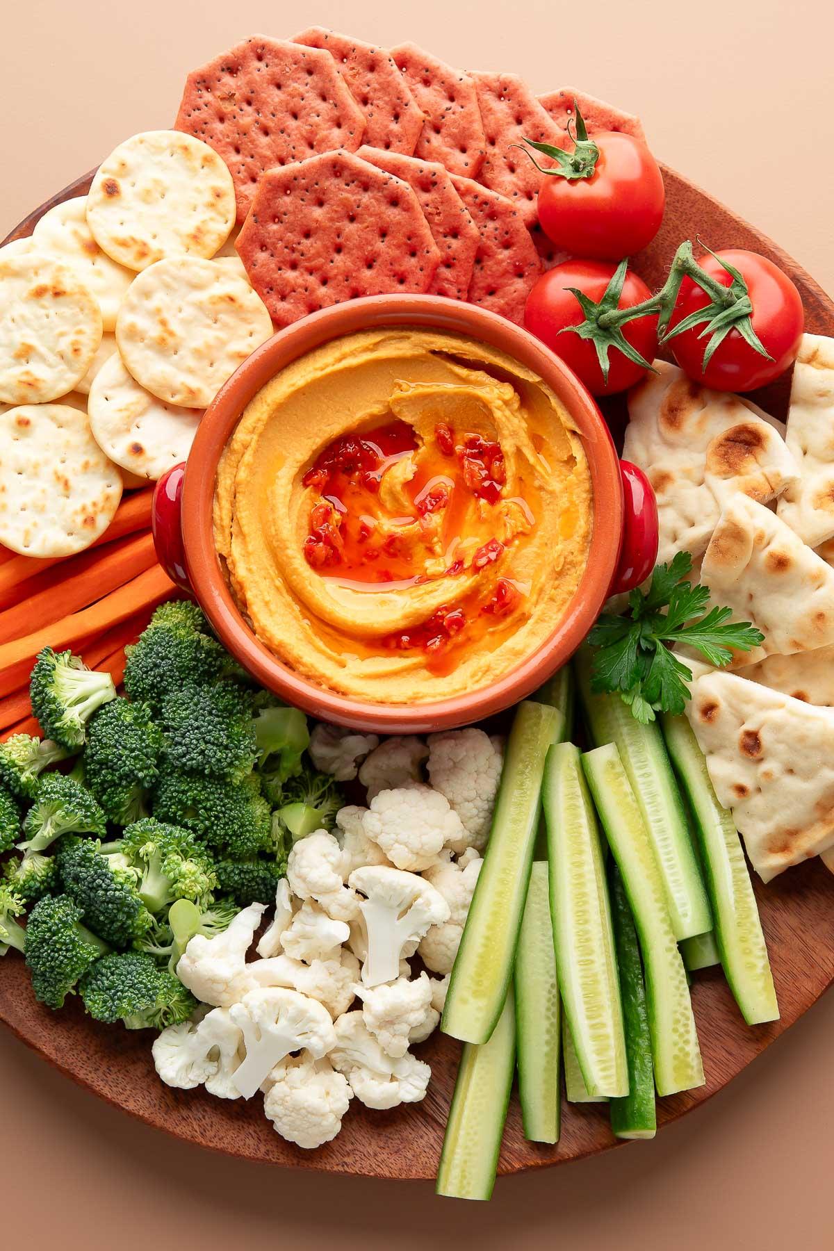 A rustic wooden board, laden with a bowl of creamy hummus and a pile of warm roasted sweet potato wedges.  Garnished with fresh herbs.