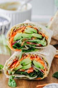 A person assembling a leafy greens and hummus wrap
