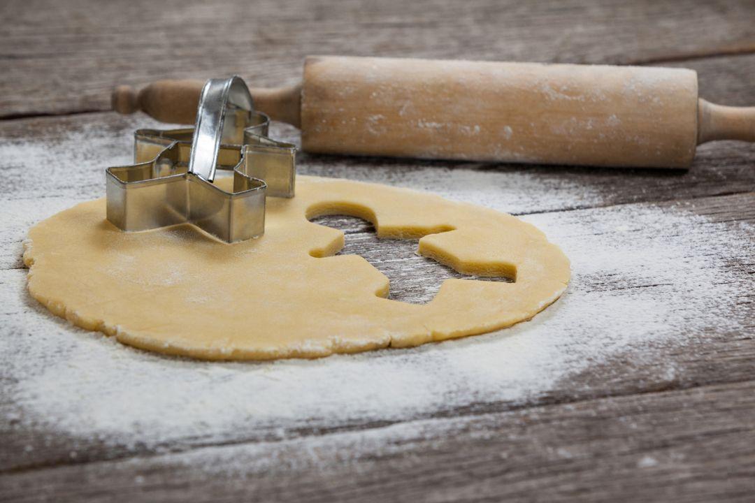 overhead shot of gingerbread cookie dough being rolled out on a floured surface with a rolling pin and cookie cutters
