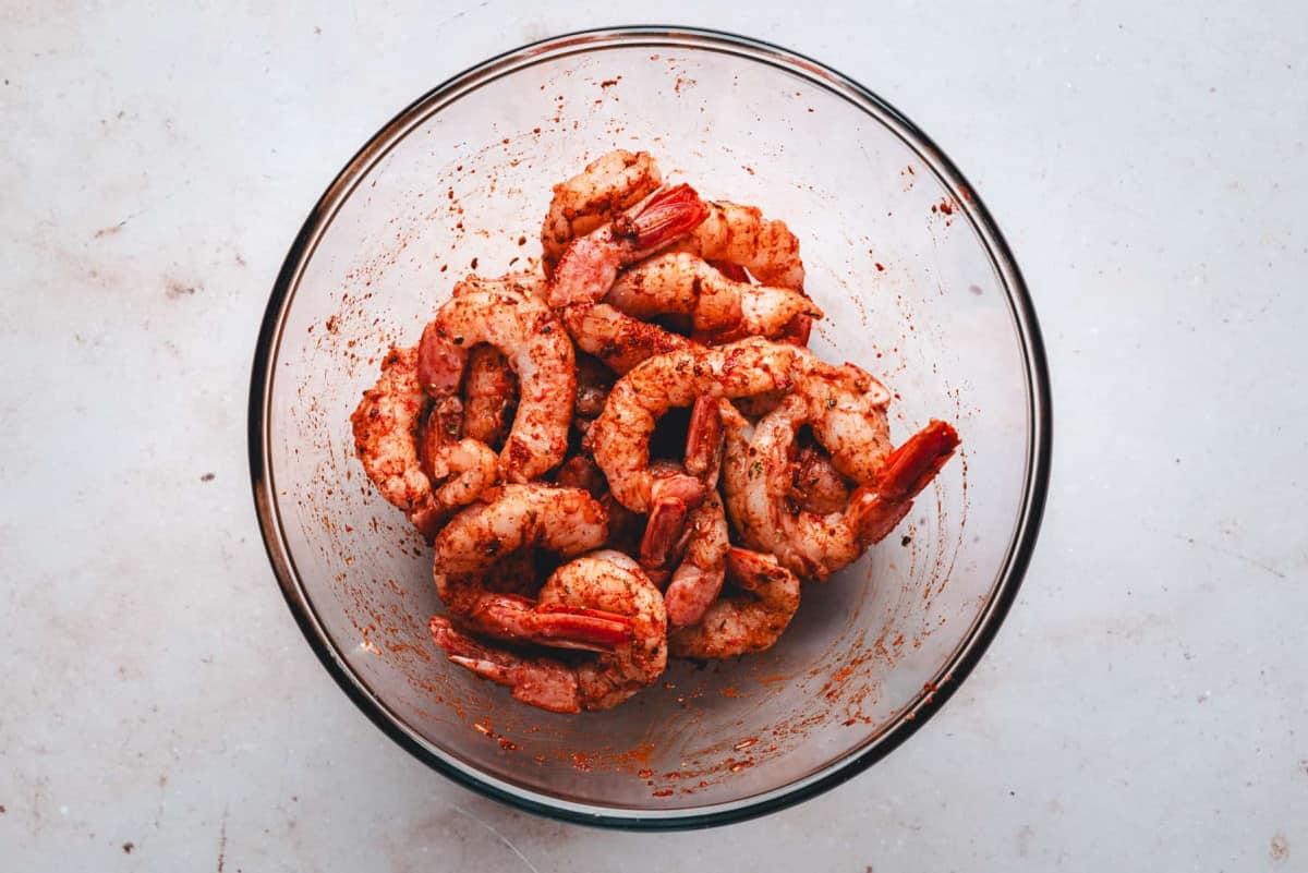 close up shot of uncooked shrimp being tossed in a bowl with spices