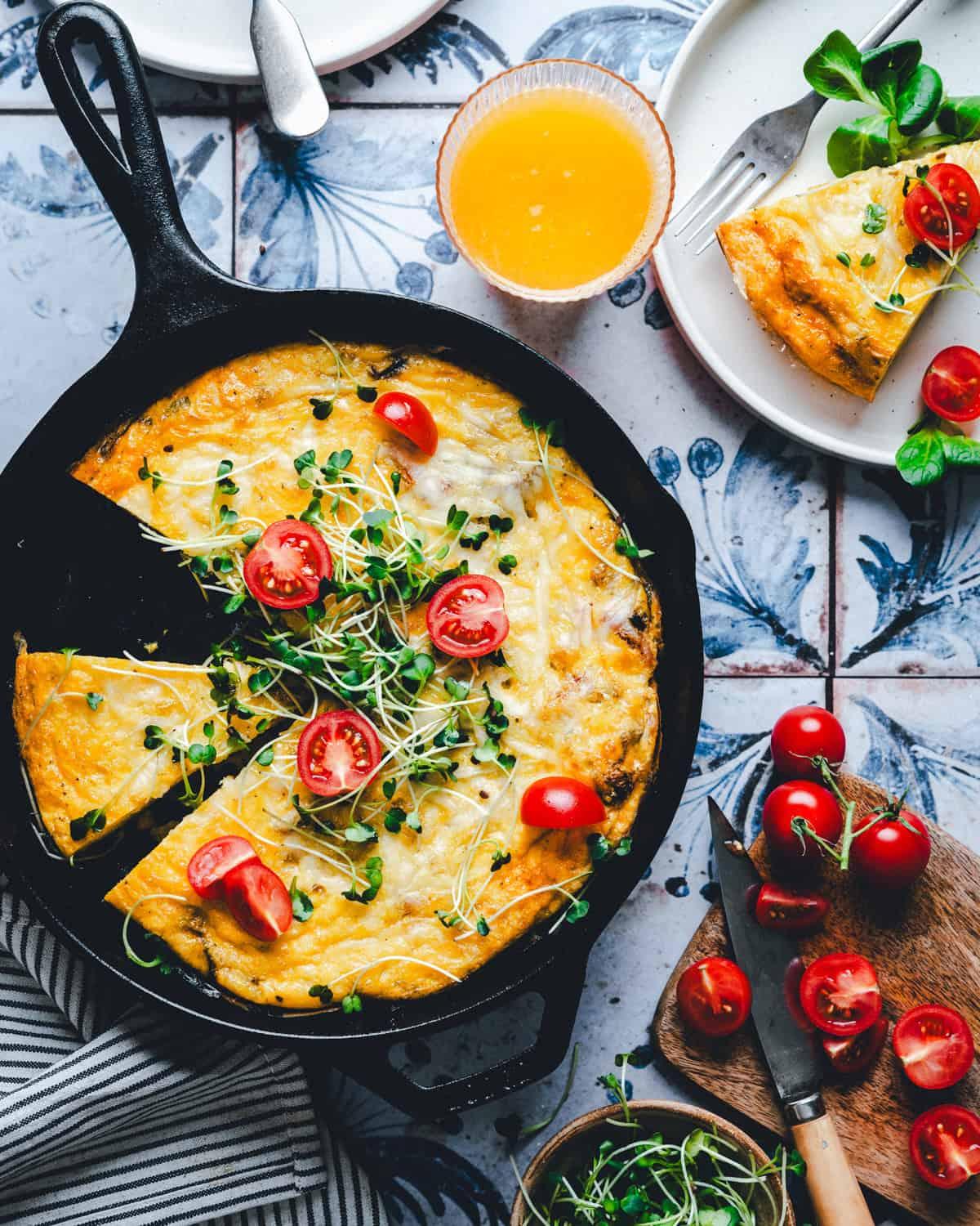 an overhead shot of a colorful frittata with various leftover ingredients visible, sitting on a wooden cutting board