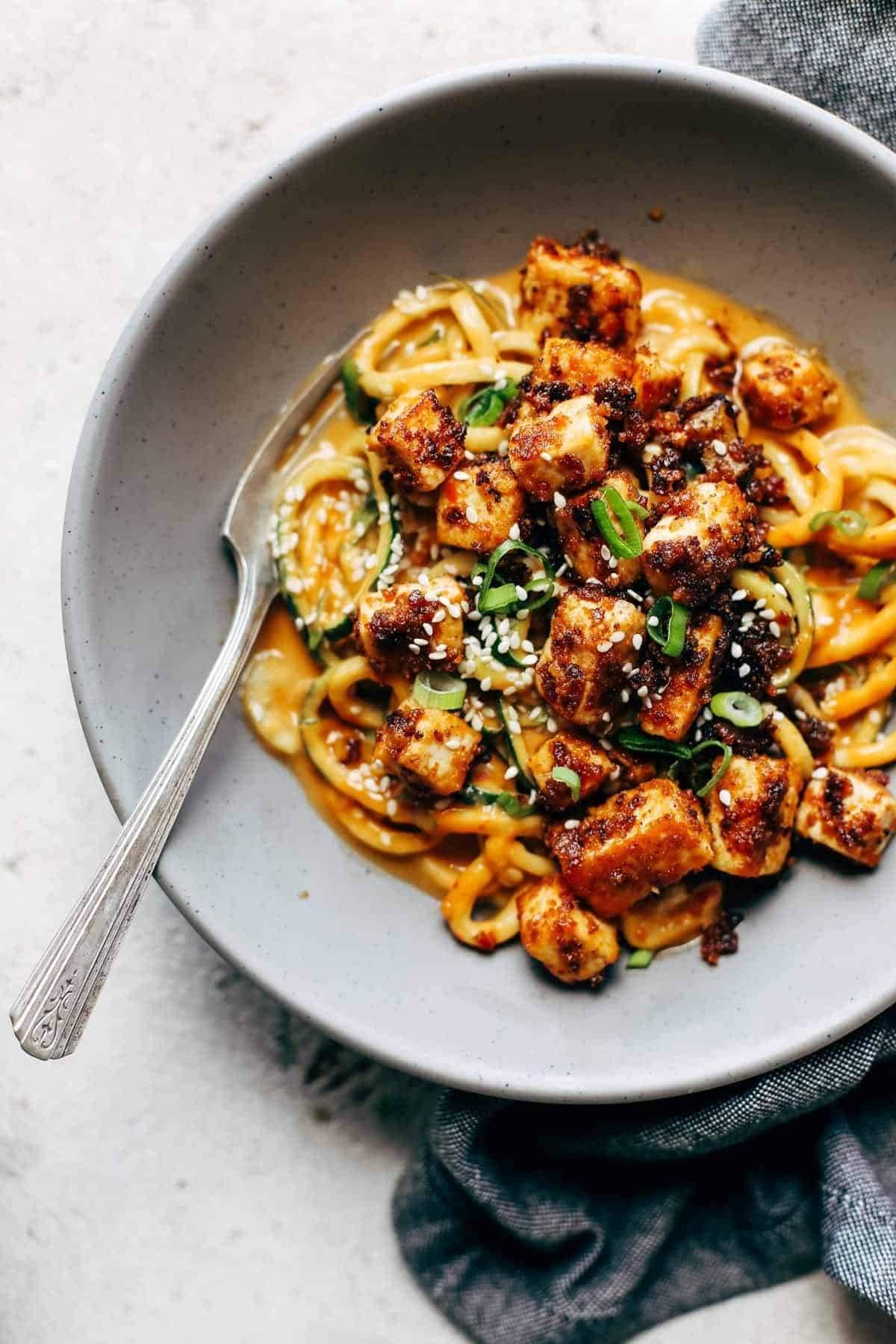 a plate of spicy peanut keto zucchini noodles with tofu topped with sesame seeds and chopped peanuts