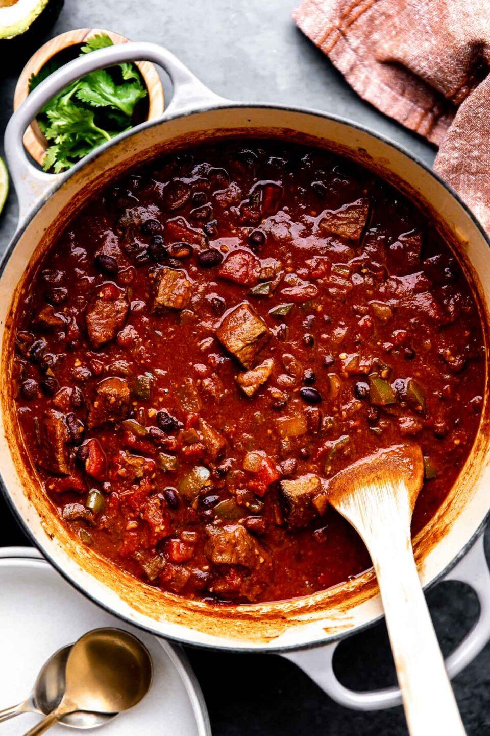 Serving spoon lifting a piece of tender chili-pepper beef from a pot, steam, focus on texture and rich color