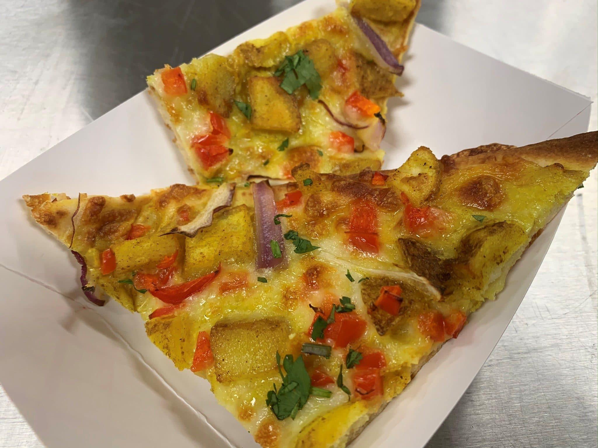 Overhead shot of a Bombay Potato Curry Pizza on a wooden board, surrounded by ingredients like potatoes, spices, and cilantro