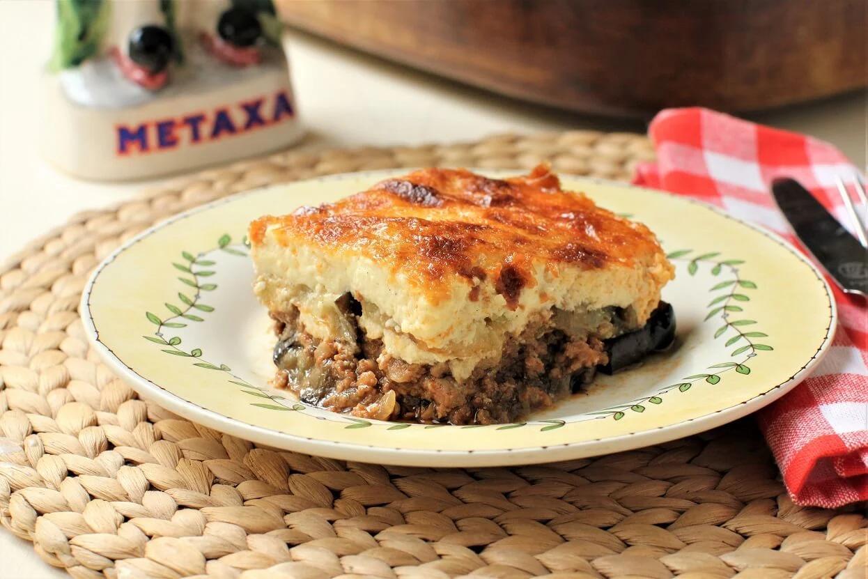 A rustic, mouthwatering image of moussaka with a rich red wine sauce, showcasing the layered potato and meat filling.