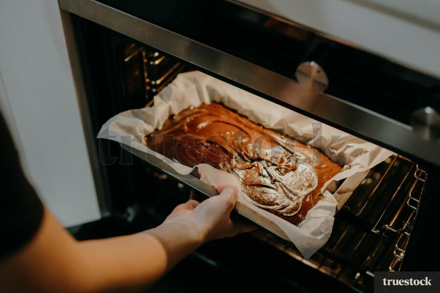 Hands placing sour patch kid brownies into the oven