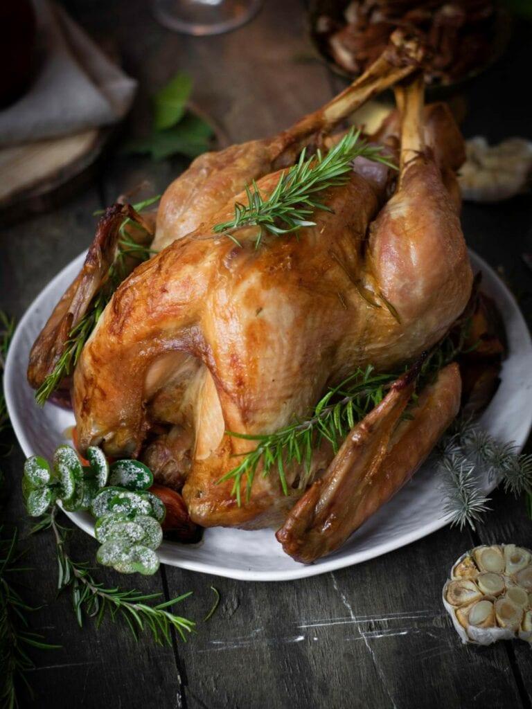 Whole roasted turkey garnished with garlic, rosemary, and lemons, on a festive dining table, golden brown and juicy