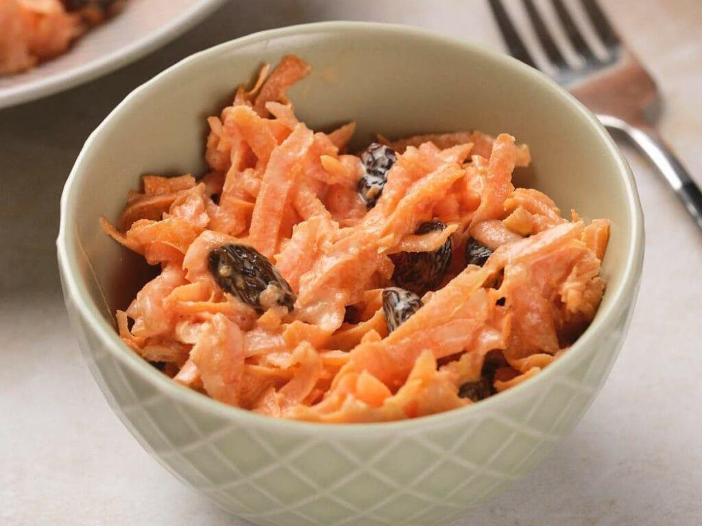 a close-up shot of someone mixing the carrot and raisin salad with a fork, showcasing the texture and ingredients
