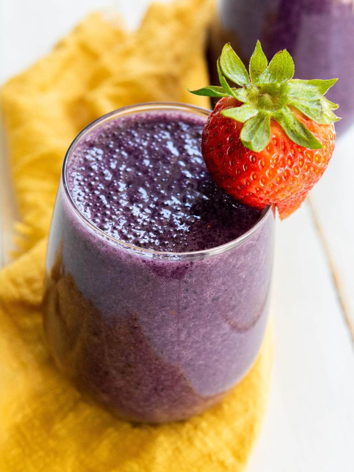 summer berry smoothie with maple syrup being poured in, garnished with fresh berries