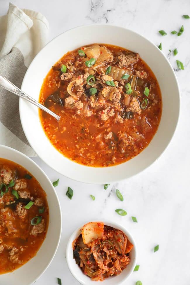 a hand stirring keto spicy kimchi soup in a pot