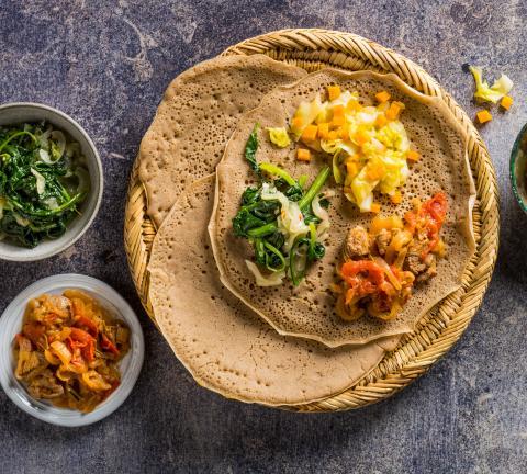 Close-up shot of a slice of Injera Bruschetta showing the texture of the crispy injera and the topping.