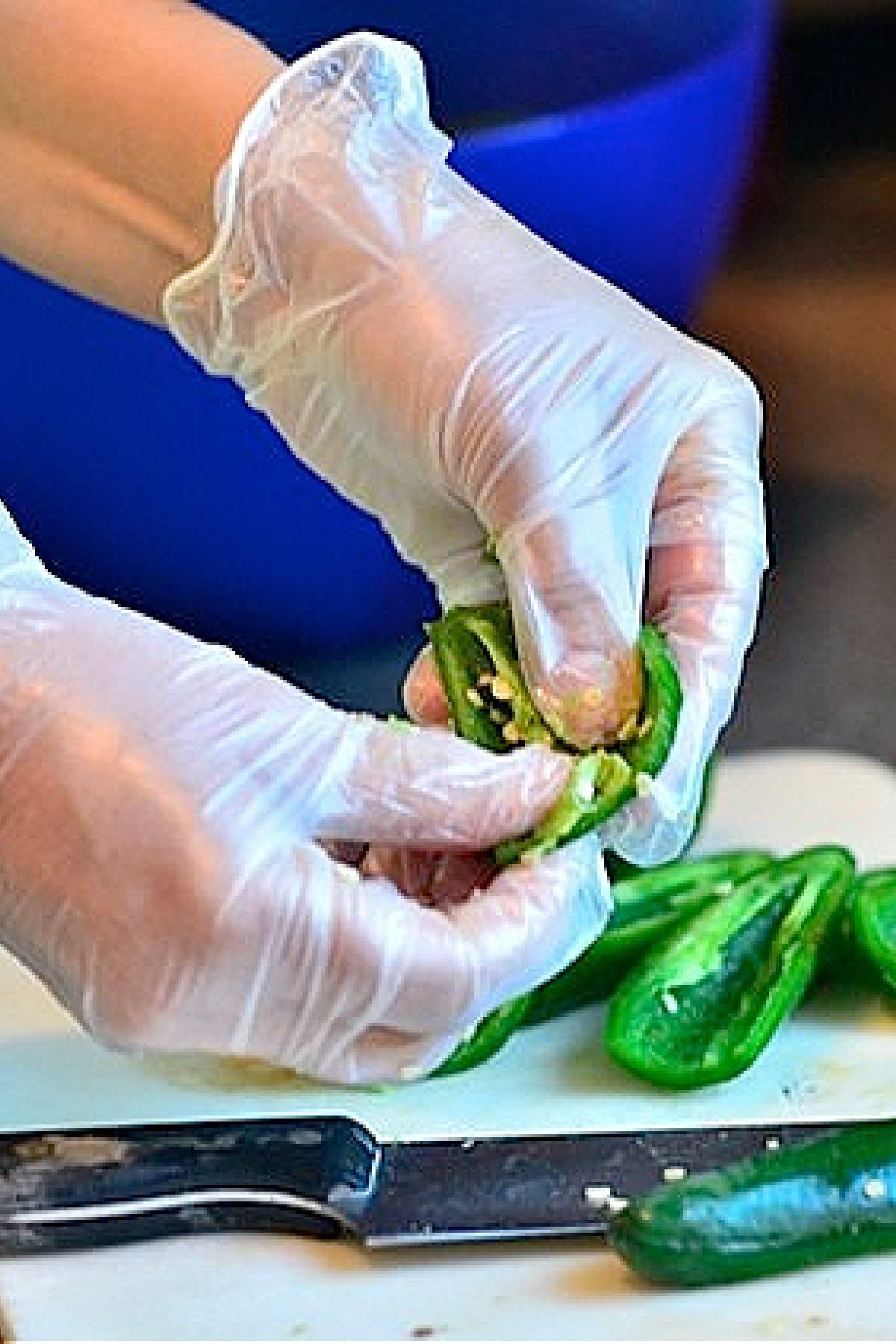 Hands wearing gloves slicing fresh jalapeños on a cutting board