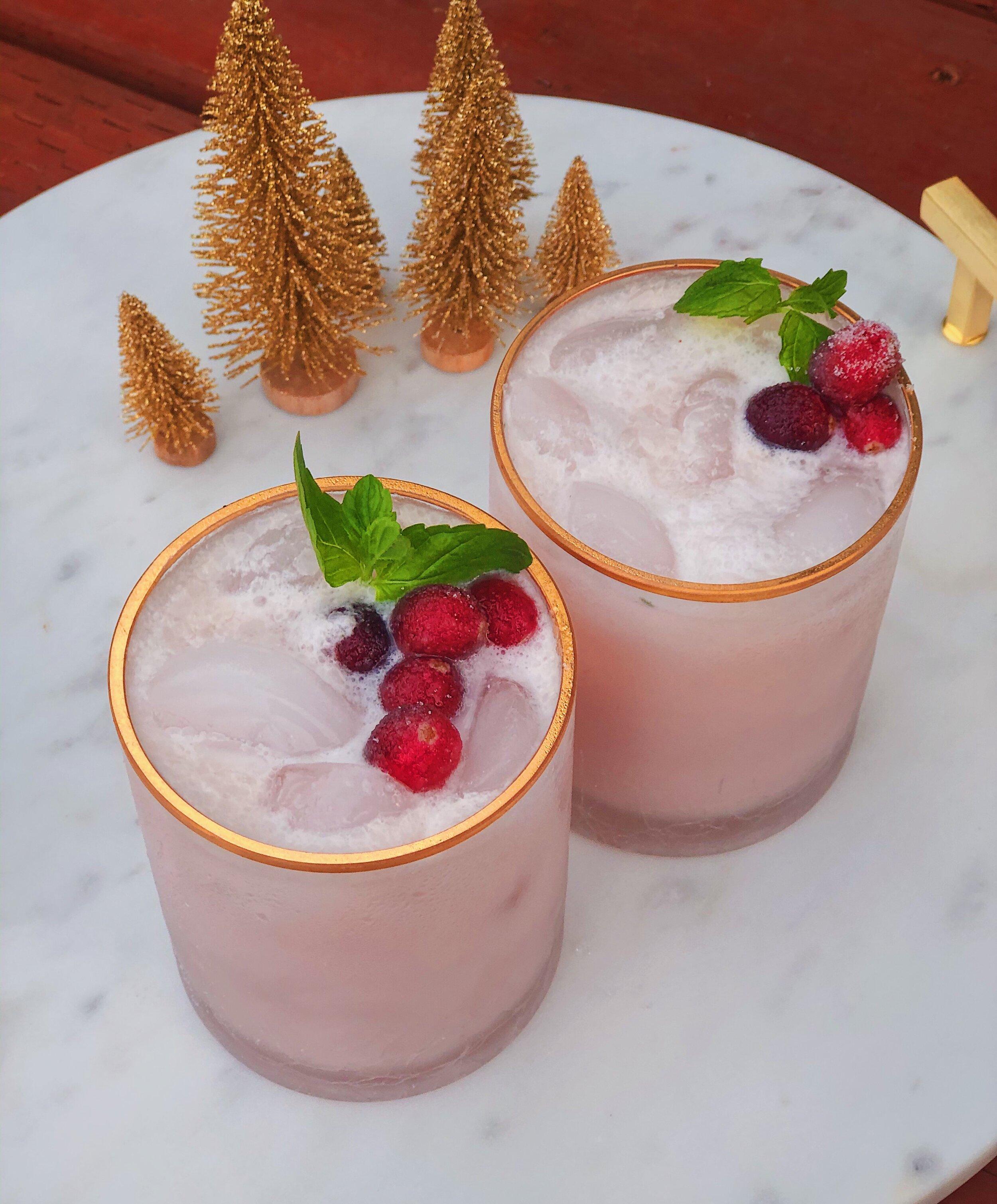 hands holding a frosty coconut mojito with blurry holiday decorations in the background