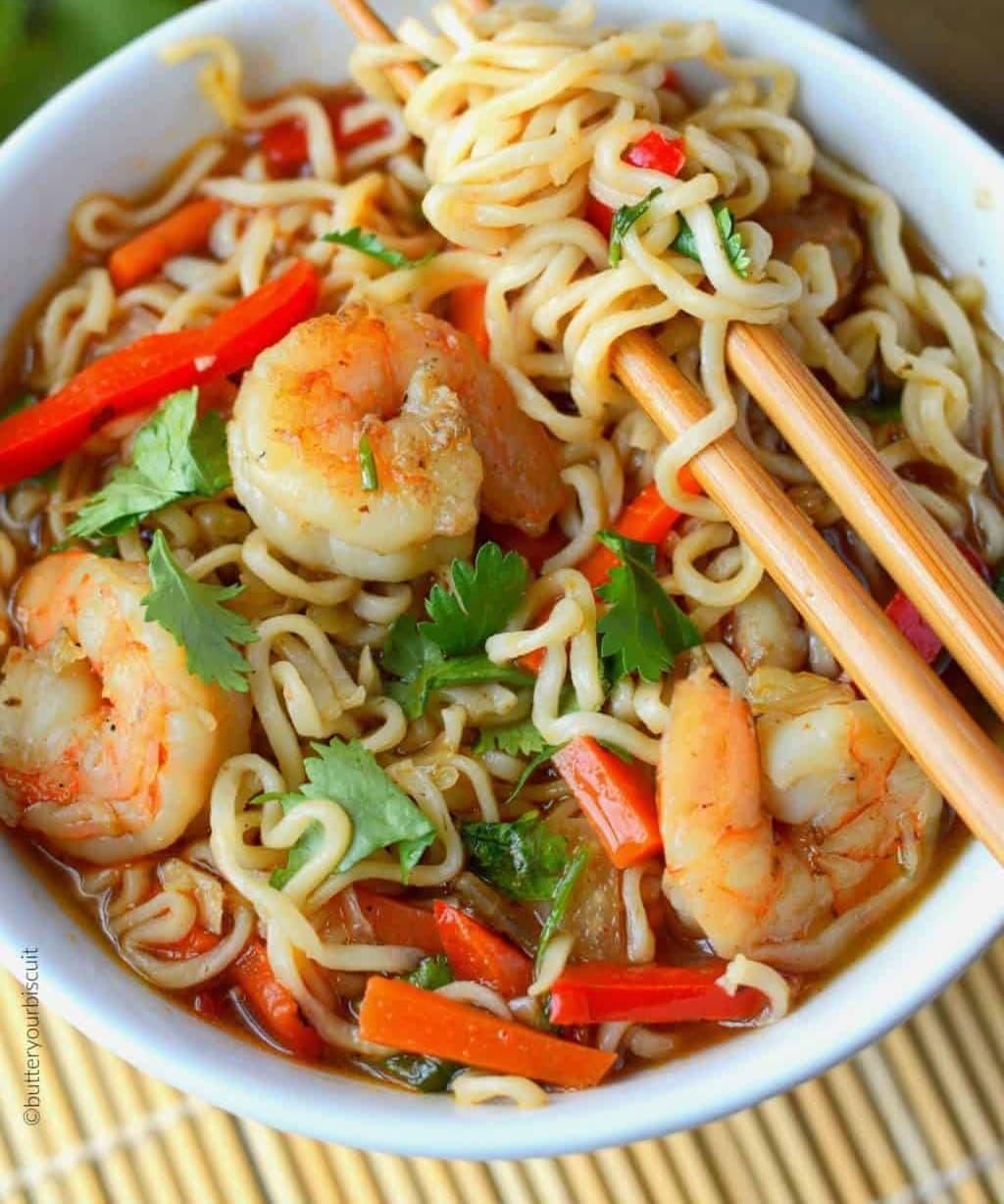 a hand sprinkling cilantro over a bowl of spicy shrimp ramen