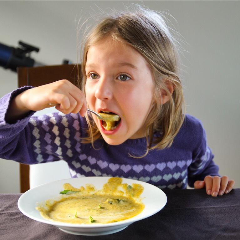 a smiling child eating a broccoli cheddar bite