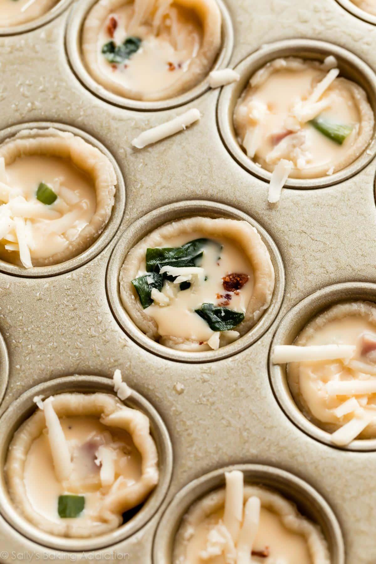 Hands arranging various fillings into mini quiche crusts before baking