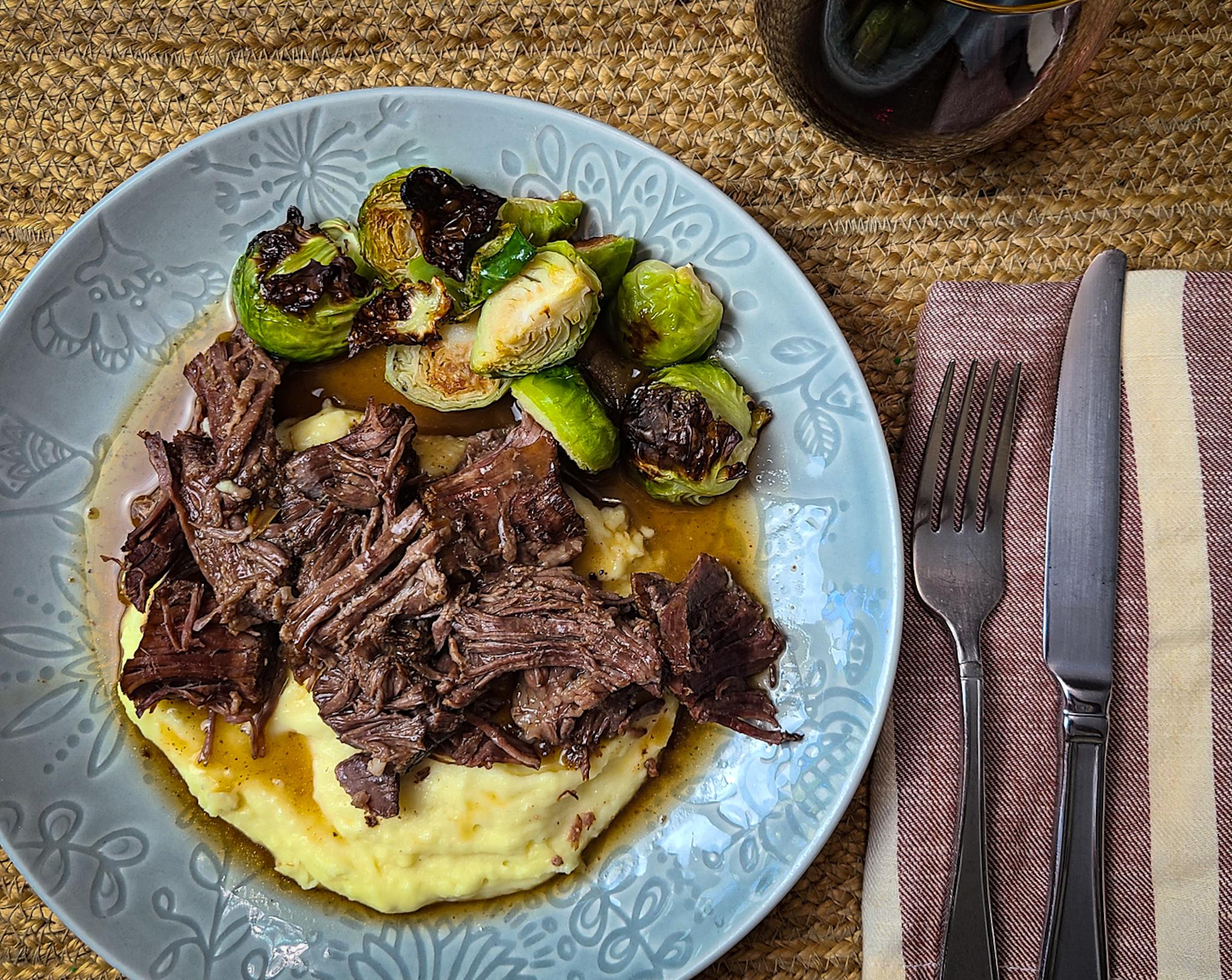 Hands shredding tender chili-pepper beef roast with a fork, rich gravy visible