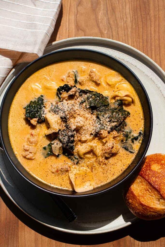 A rustic bowl of pumpkin soup with Italian sausage and kale, garnished with a swirl of cream and a sprinkle of parmesan cheese.