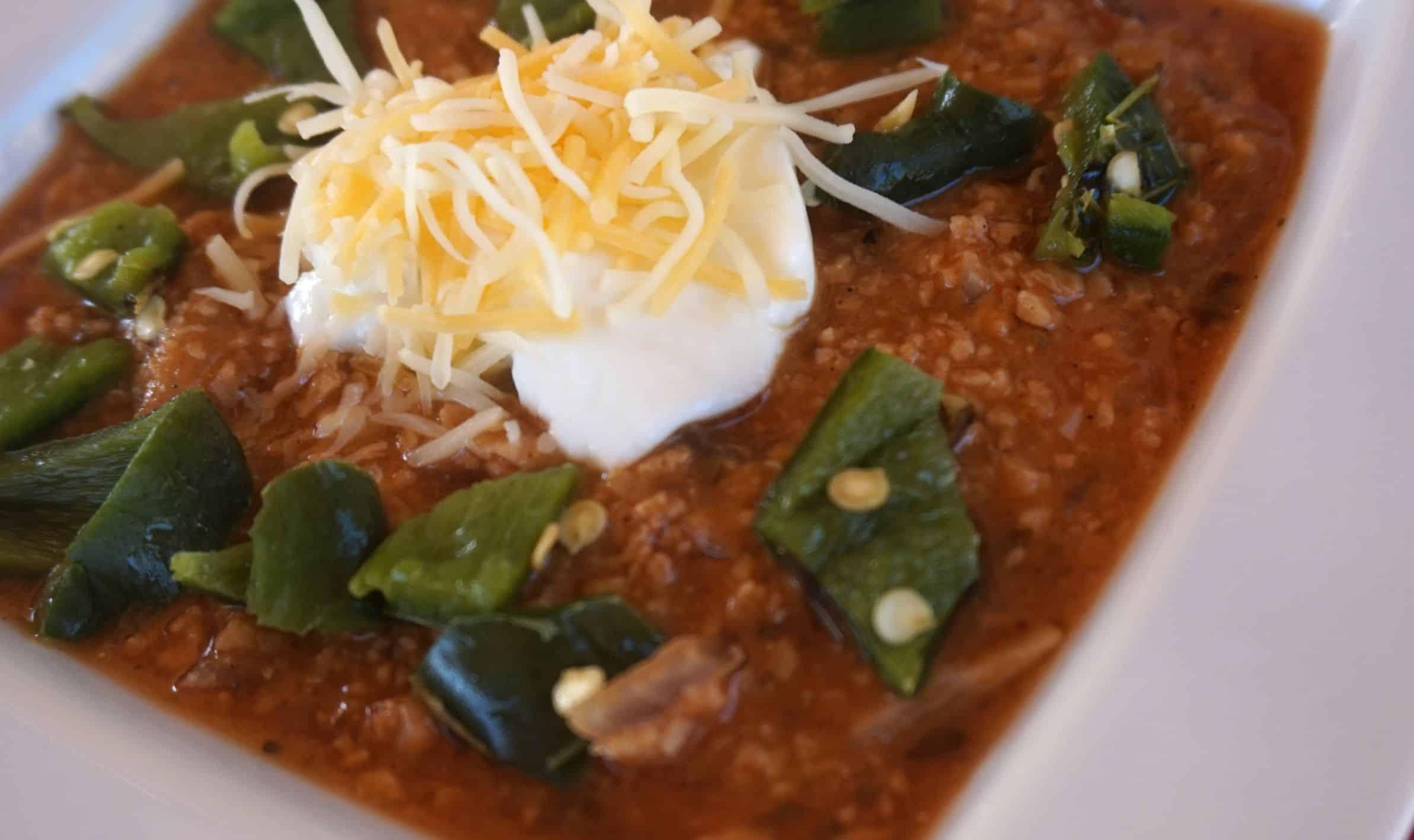 Rustic smoky firehouse chili pot with steam, topped with cheese and jalapeños, close-up, warm lighting