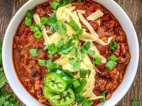 Close-up of browned ground beef in a Dutch oven with chopped onions, bell peppers, and jalapeños, ready for spices