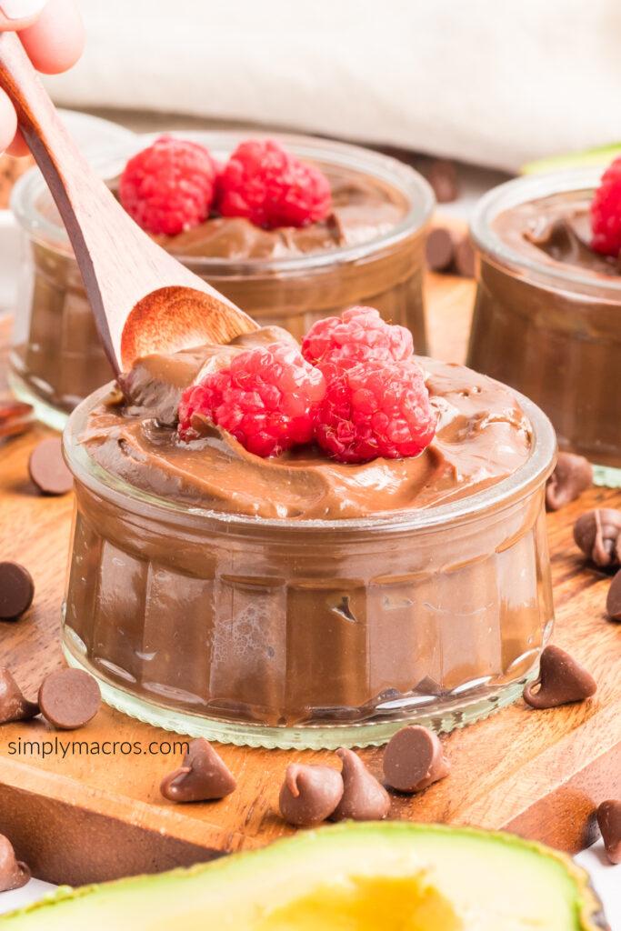 overhead shot of several glasses of chocolate avocado mousse with spoons, garnished with raspberries
