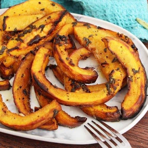 roasted pumpkin cubes on a baking sheet with fresh sage leaves