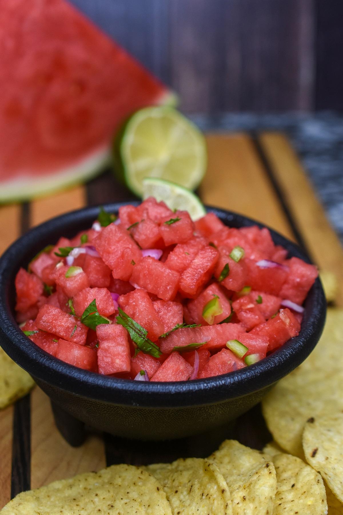 a bowl of spicy watermelon and black bean salsa with tortilla chips on a wooden table