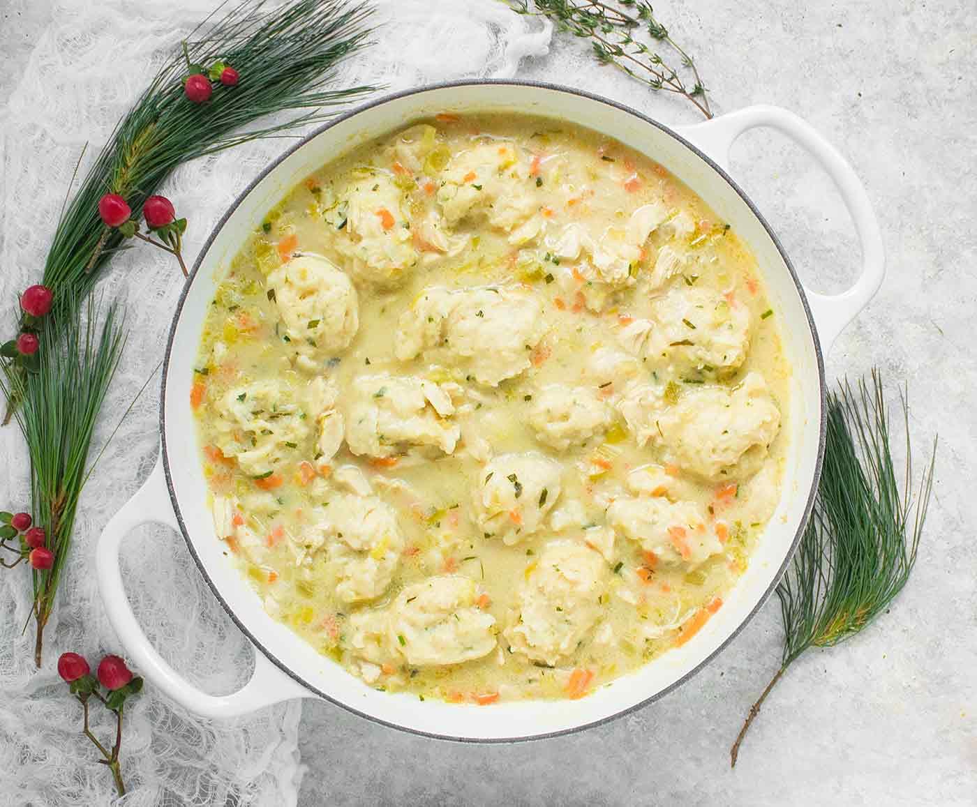 Smiling woman holding a warm, cozy bowl of chicken and dumplings by a window on a cold day.