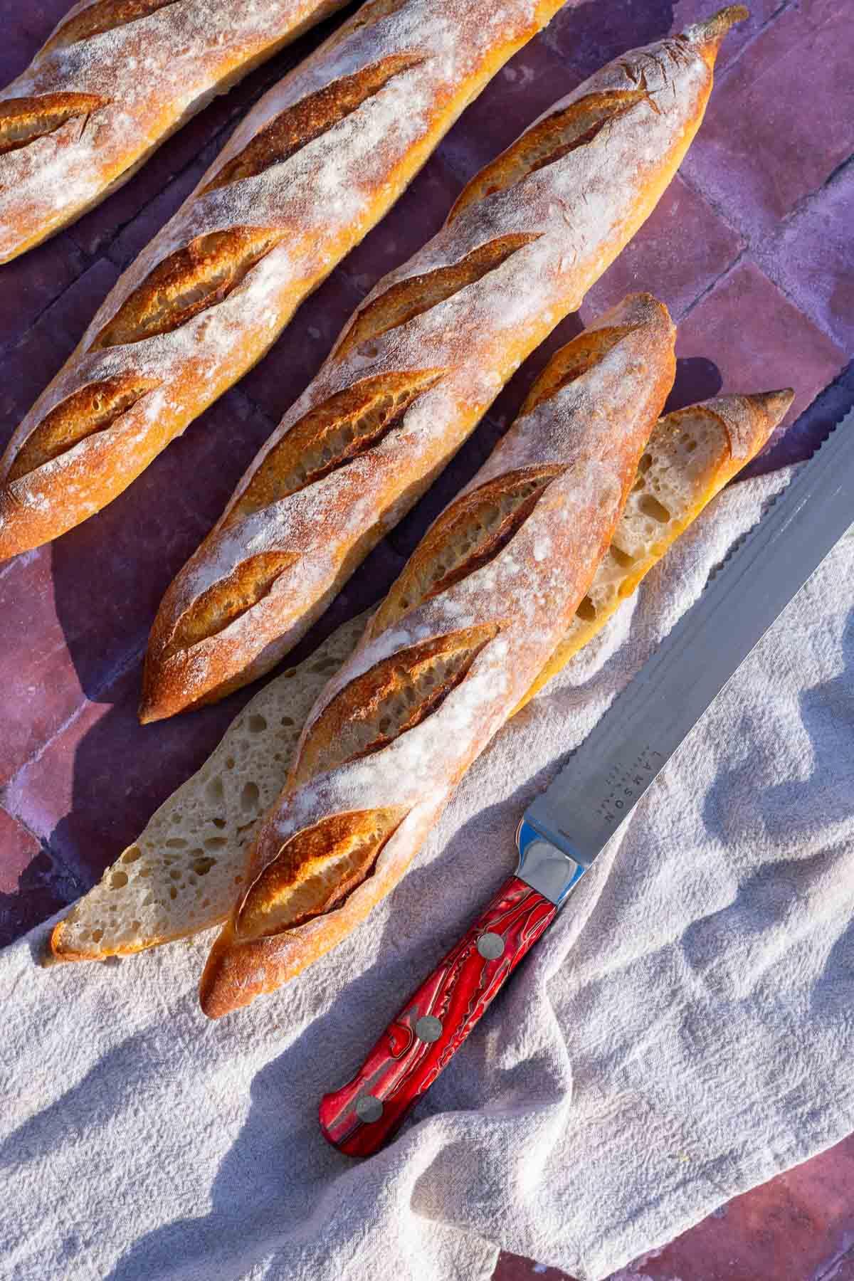 freshly baked sourdough baguettes on a wooden cutting board with a knife