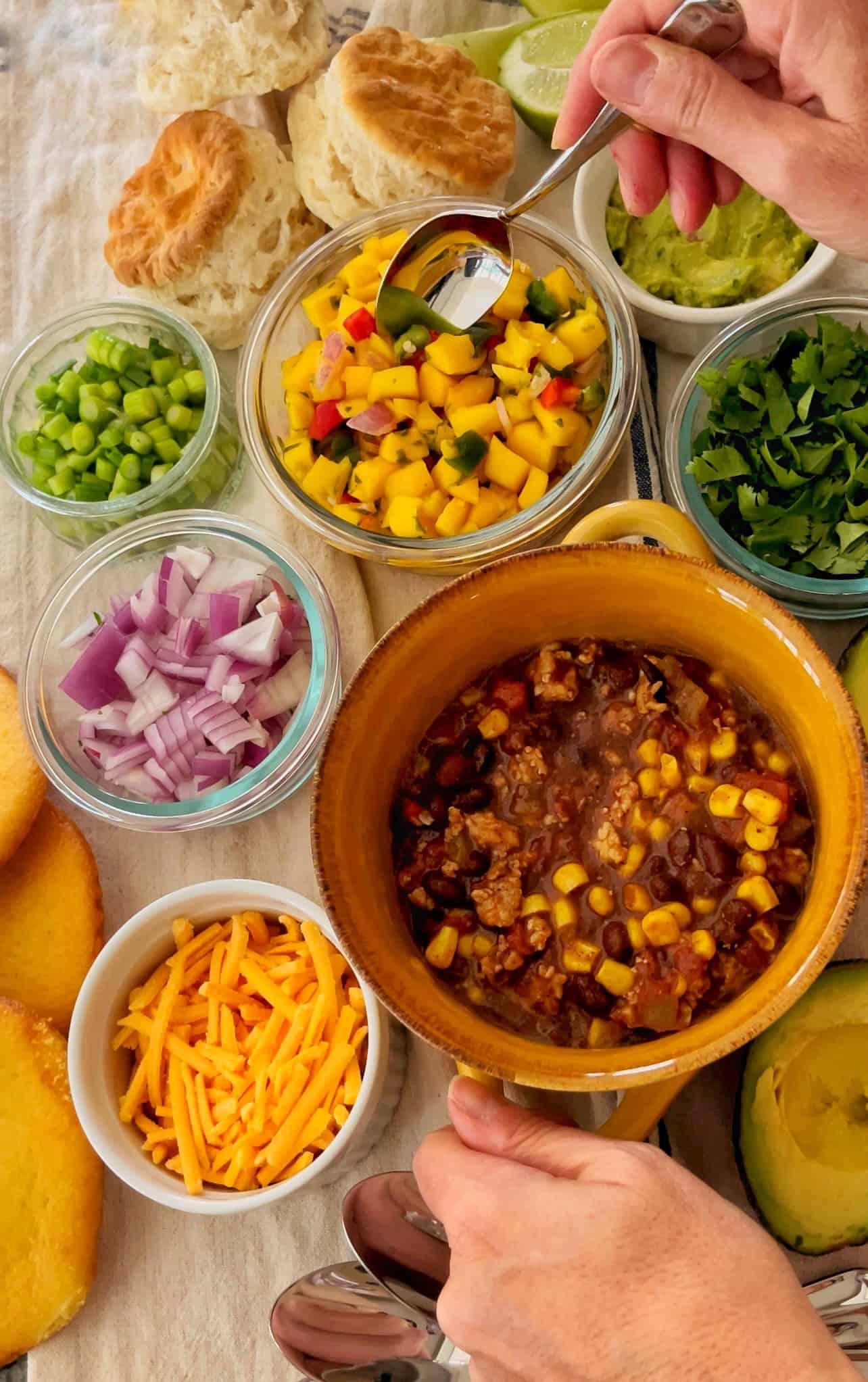 A table set for a chili cook-off with various bowls of chili and people enjoying it.