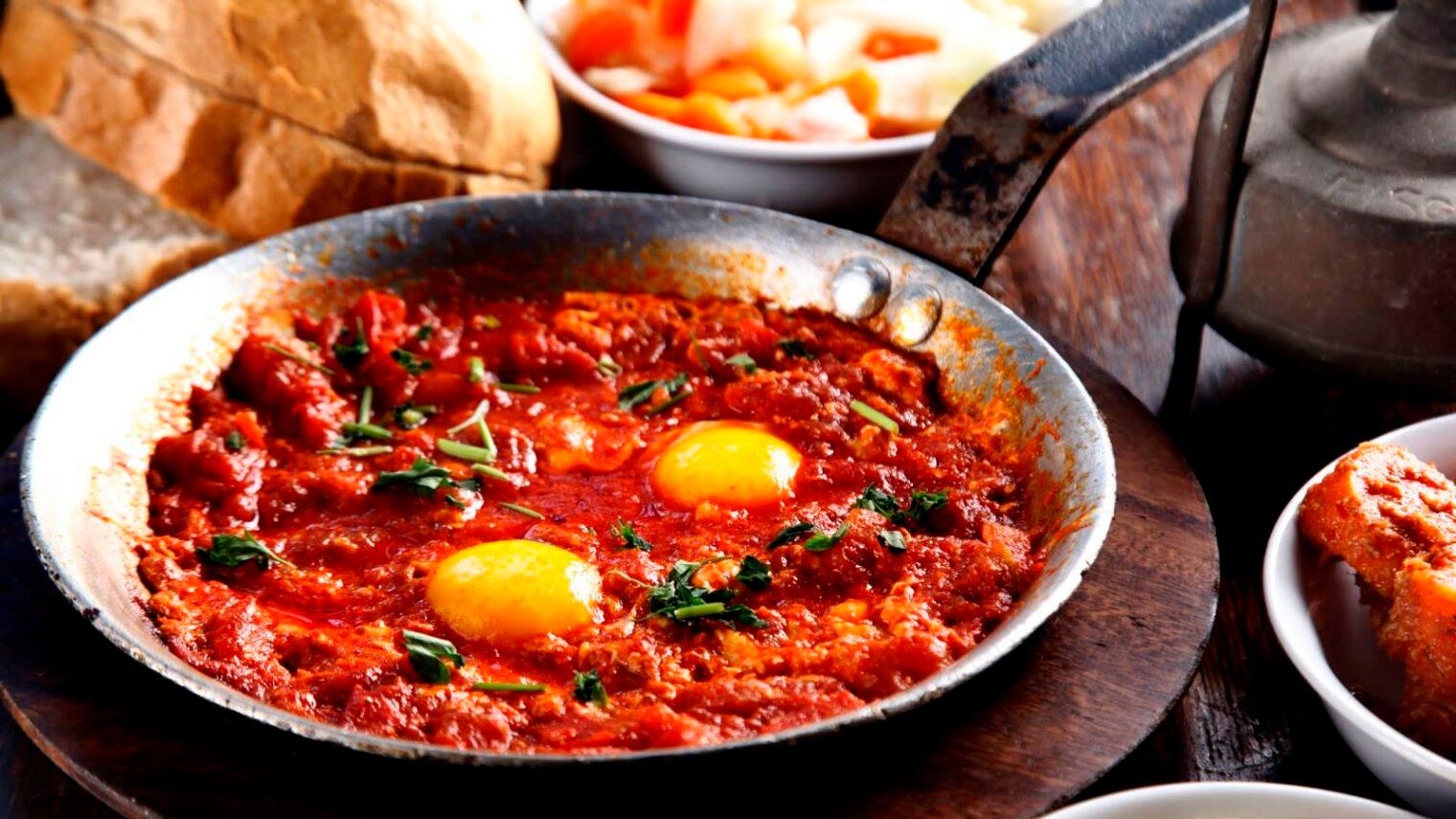 A person scooping Shakshuka with Raspberries and Pistachios onto a plate