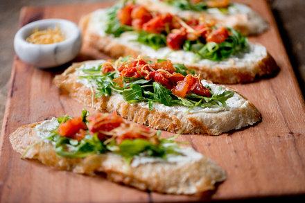Person casually arranging a platter of whipped feta dip, roasted tomatoes, and bread, warm lighting
