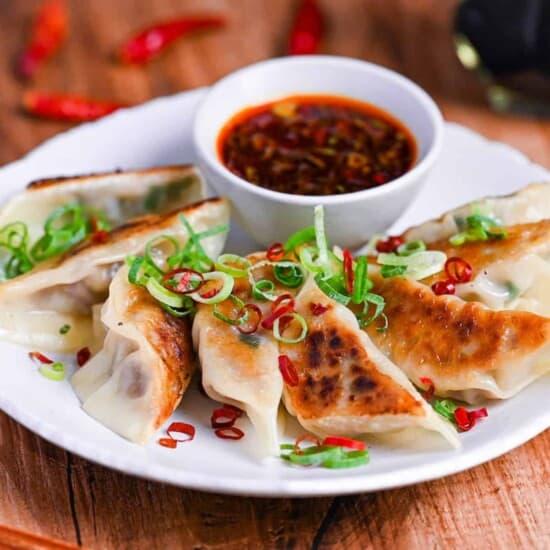 A plate of freshly steamed and pan-fried spicy beef and cabbage dumplings with a dipping sauce