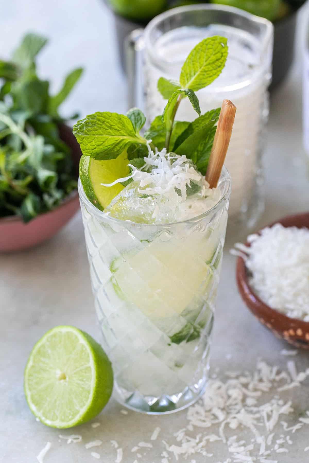 close up shot of a coconut mojito with fresh mint, lime wedges, and a frosted glass
