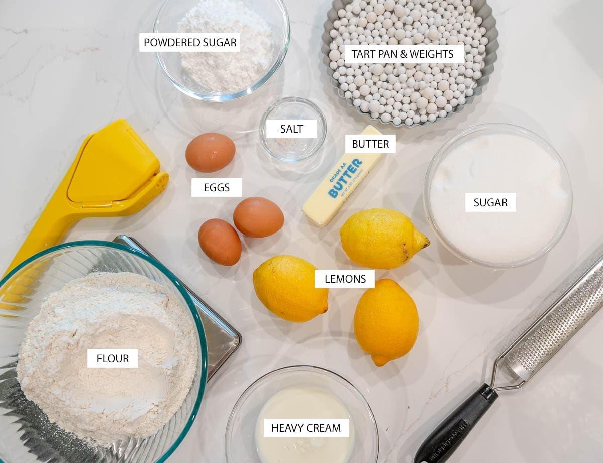 Overhead shot of lemon halves, a grater, and a whisk on a kitchen counter, ingredients for lemon tart
