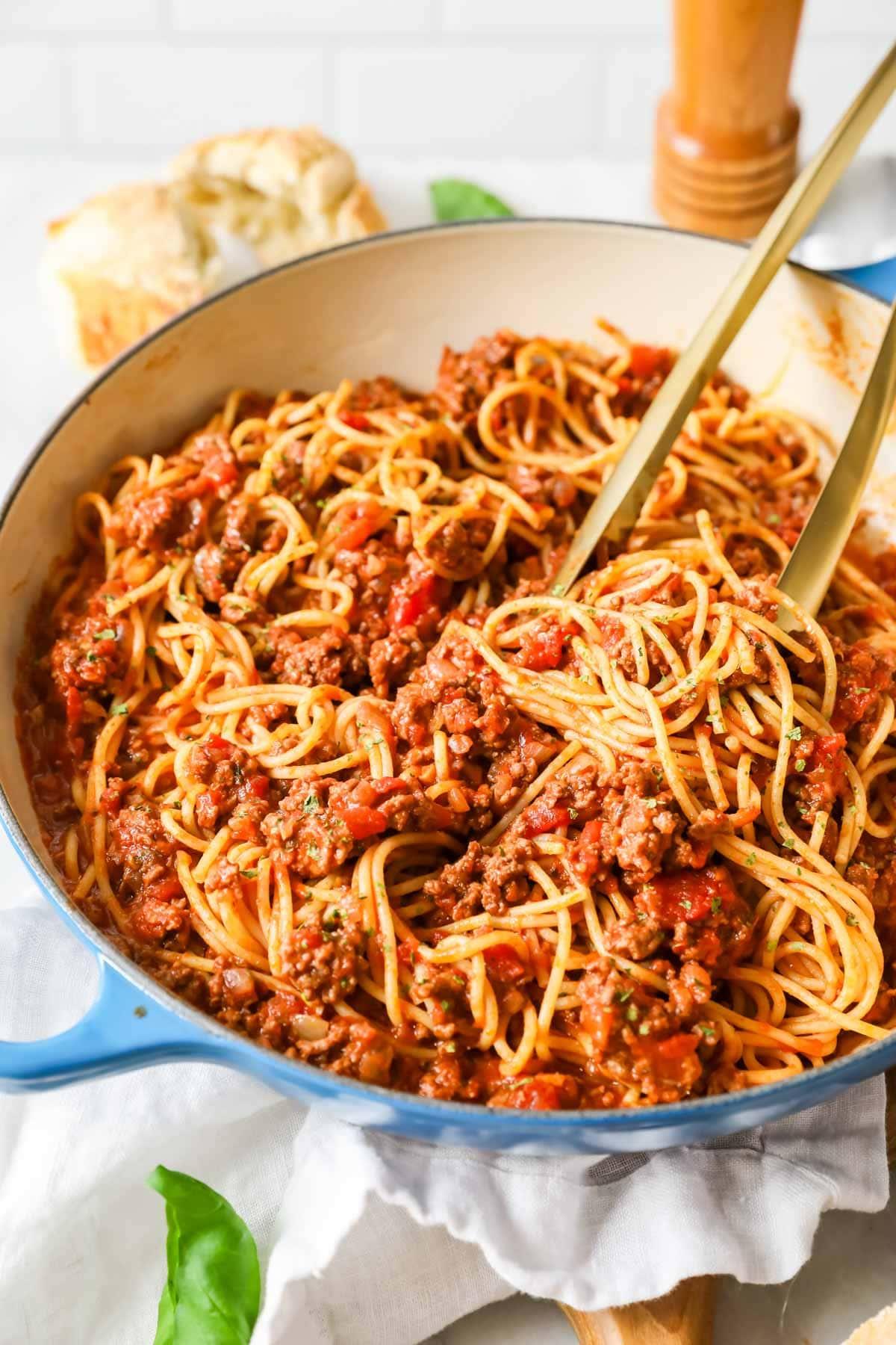 person tossing cooked pasta with beef bolognese sauce in a pot