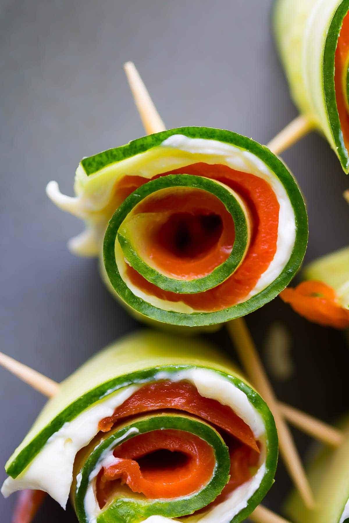 A hand assembling a smoked salmon and cucumber skewer
