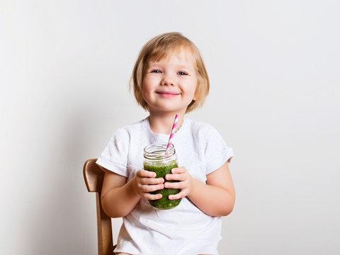 a child happily drinking a green grape smoothie with a big smile
