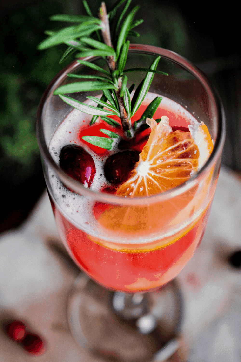 Close up of a single cranberry rosemary mimosa, showing the color and rosemary garnish