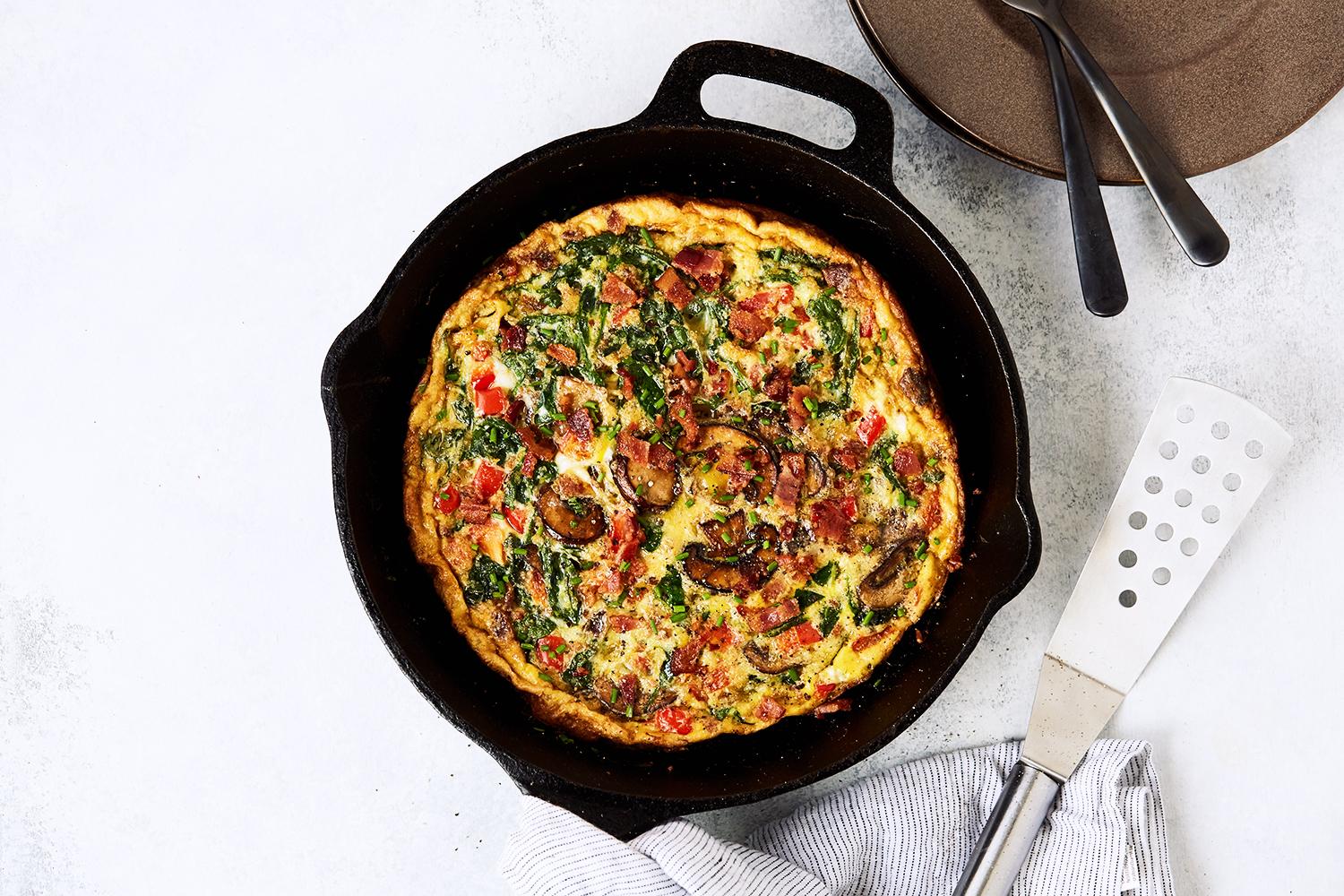 a person smiling as they pull a golden-brown frittata out of the oven
