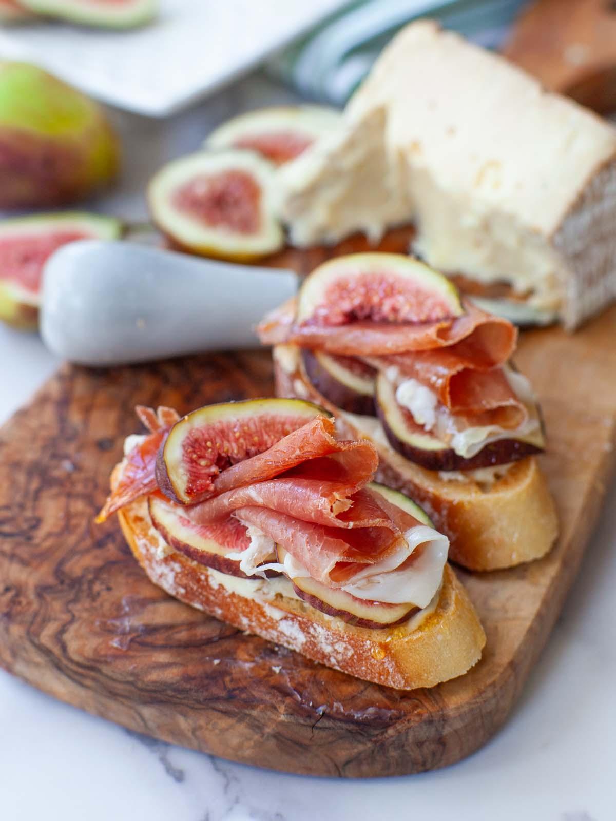 close up of prosciutto slices artfully draped on a charcuterie board next to a small bowl of fig spread