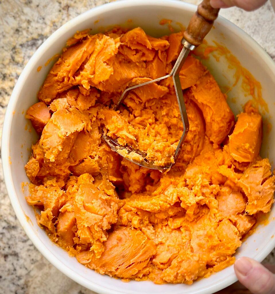 Hands mashing cooked sweet potatoes in a bowl