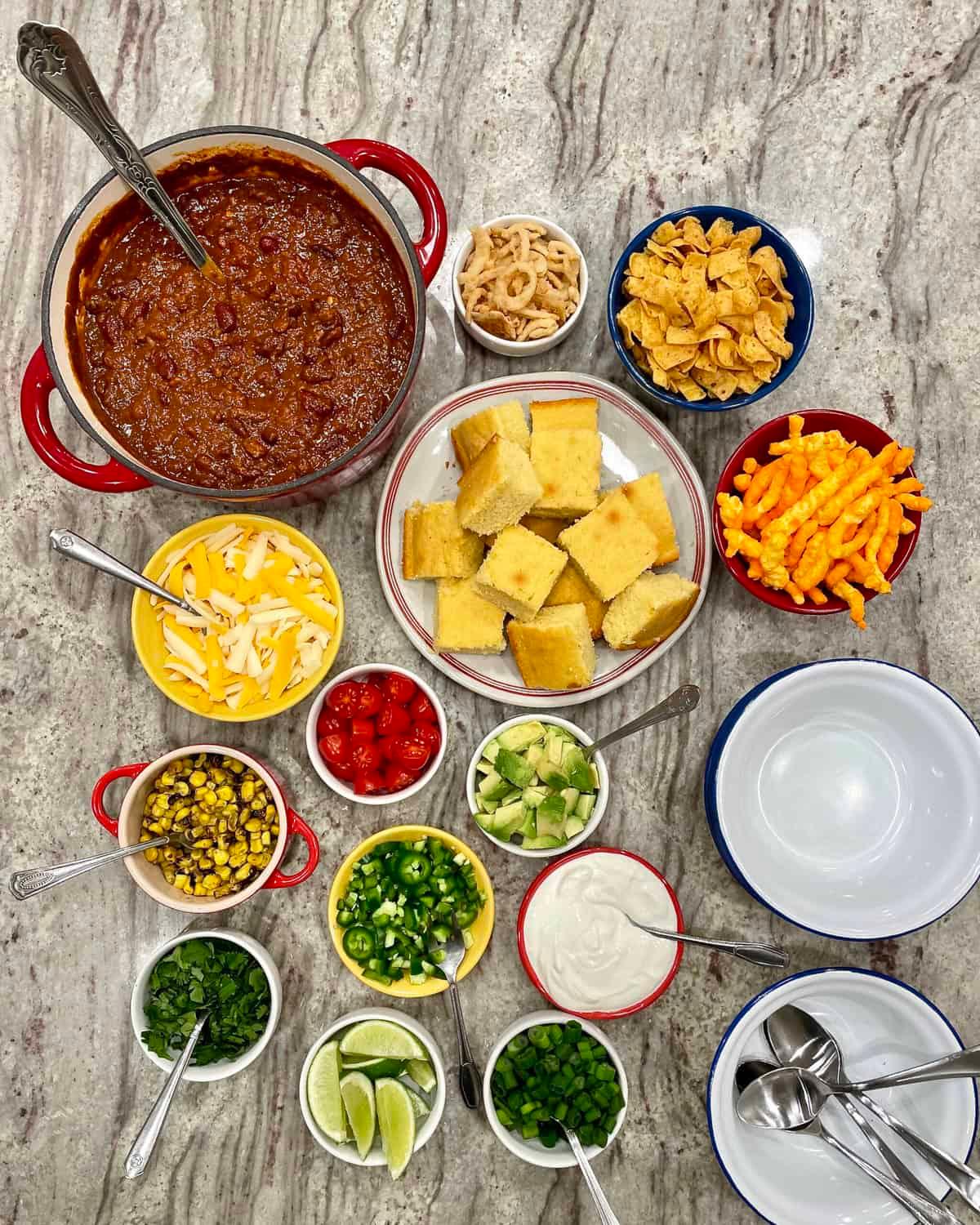 various chili toppings in small bowls, arranged around a pot of chili