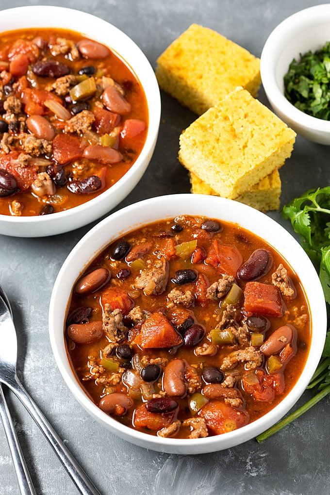 Overhead shot of a large pot of simmering chili on a stovetop with ingredients around it