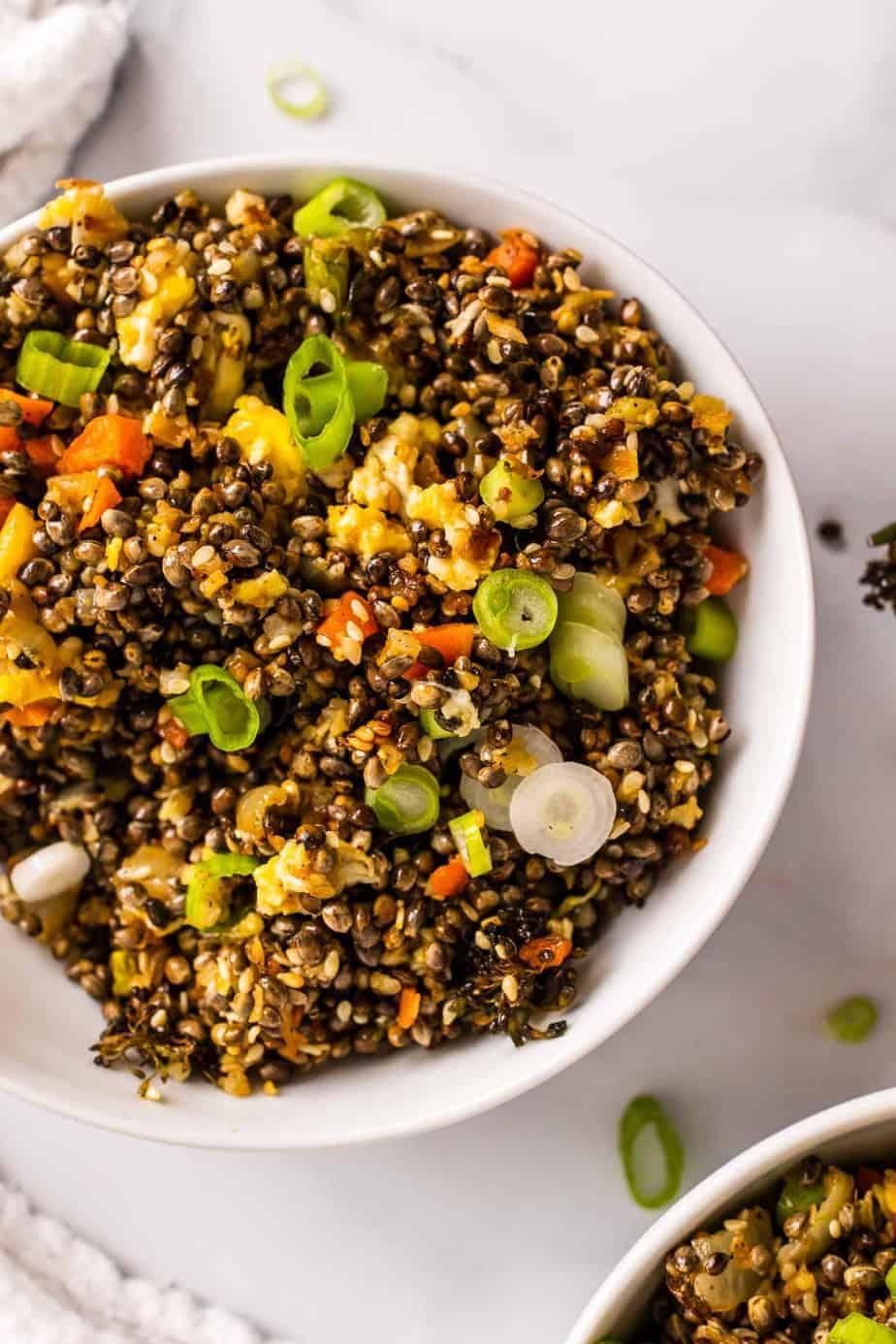close up shot of cauliflower rice with chopped hazelnuts and dark chocolate shavings in a bowl