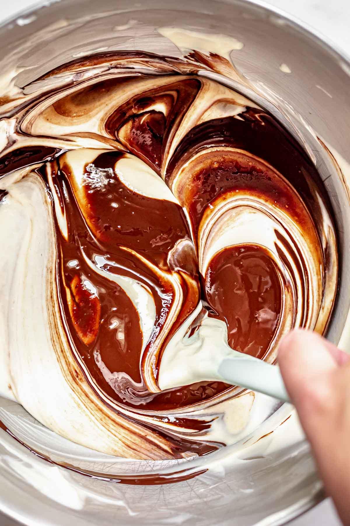 Melted dark and white chocolate being swirled together in a bowl, marbling effect