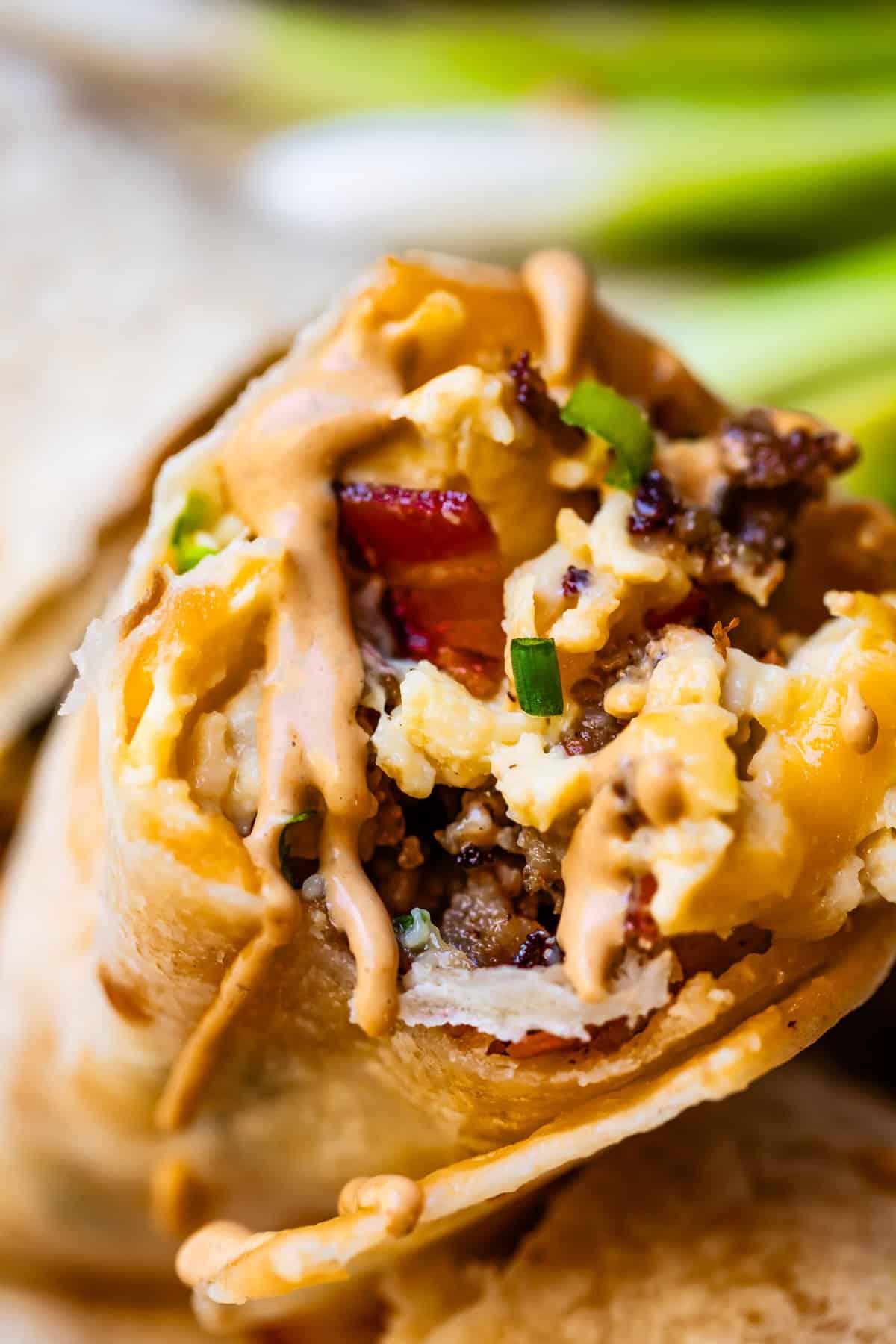 Close-up of a hand holding a plantain burrito, with toppings like sour cream and salsa