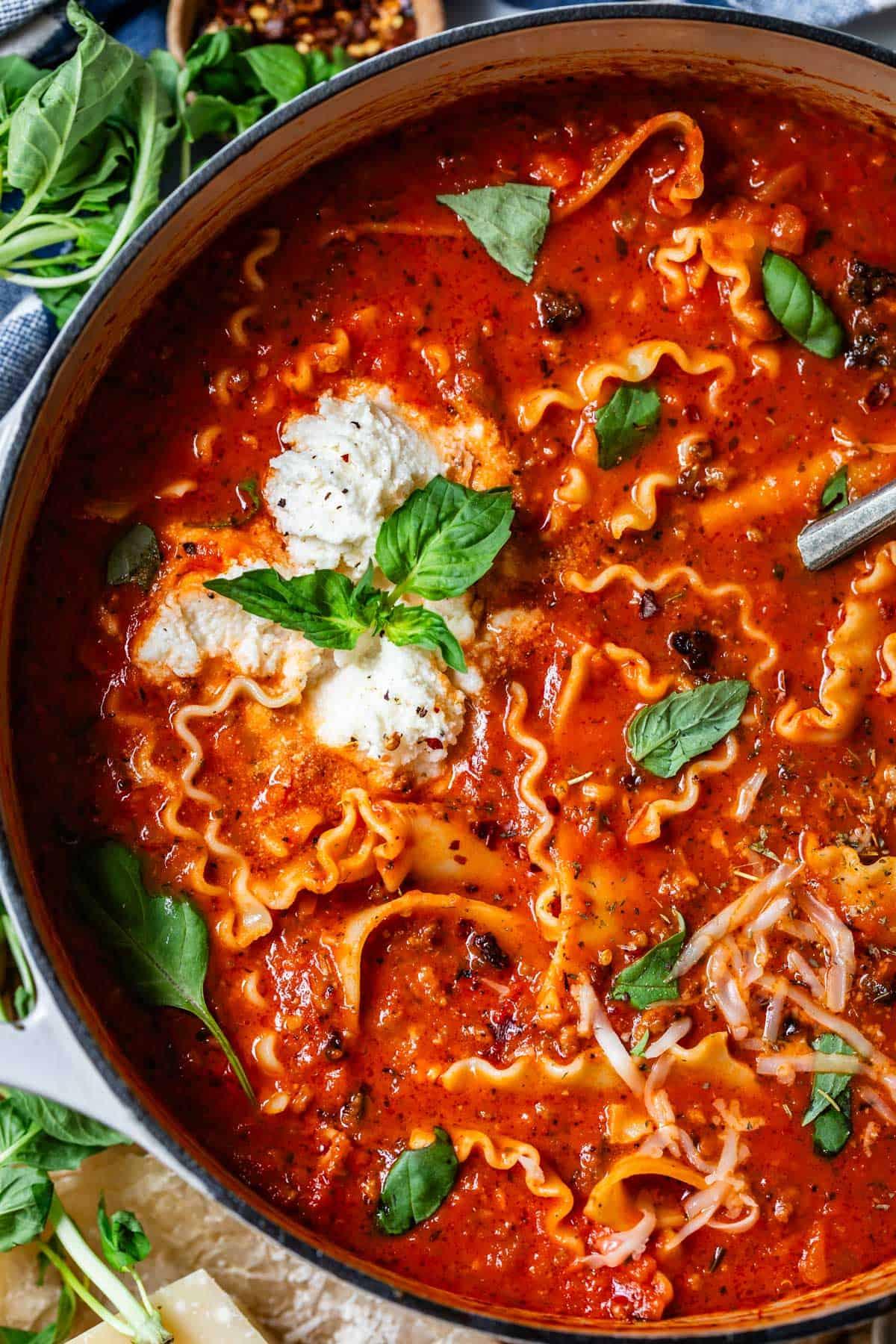 Steaming bowl of rich, cheesy lasagna soup with dollop of ricotta and fresh basil, comfort food style