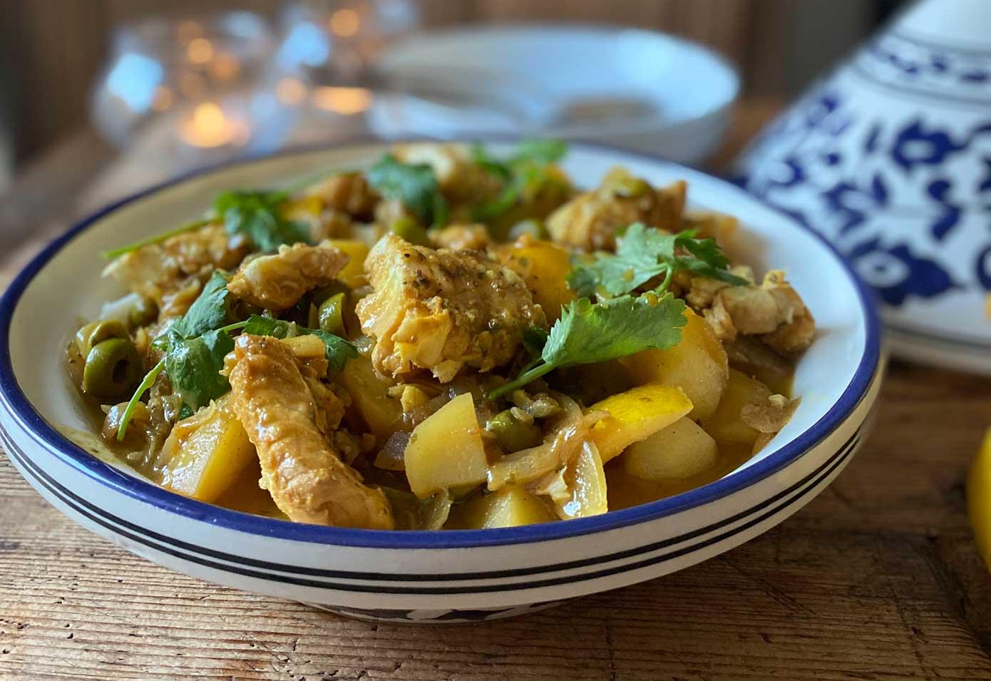 A steaming tagine pot filled with golden-hued fish tagine, garnished with fresh herbs and preserved lemons.